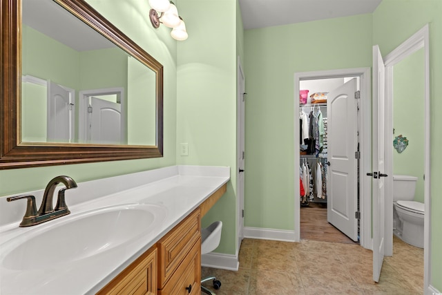 full bathroom with toilet, vanity, a walk in closet, tile patterned flooring, and baseboards
