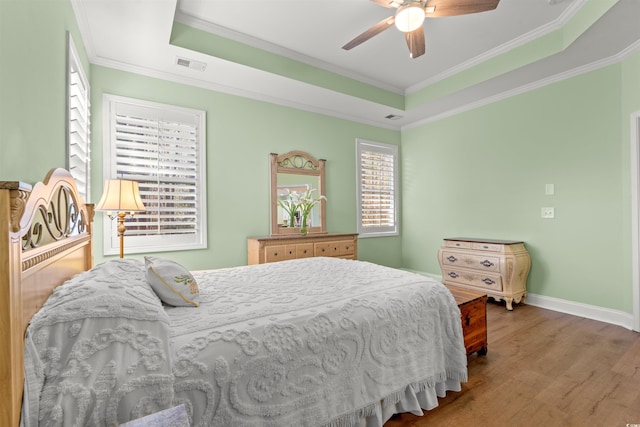 bedroom with a tray ceiling, wood finished floors, ornamental molding, baseboards, and a ceiling fan