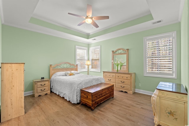 bedroom with a tray ceiling, light wood-type flooring, ornamental molding, baseboards, and ceiling fan