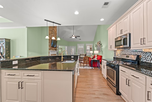 kitchen with appliances with stainless steel finishes, a sink, a ceiling fan, light wood finished floors, and tasteful backsplash