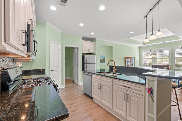 kitchen featuring a sink, appliances with stainless steel finishes, white cabinetry, hanging light fixtures, and a kitchen island with sink