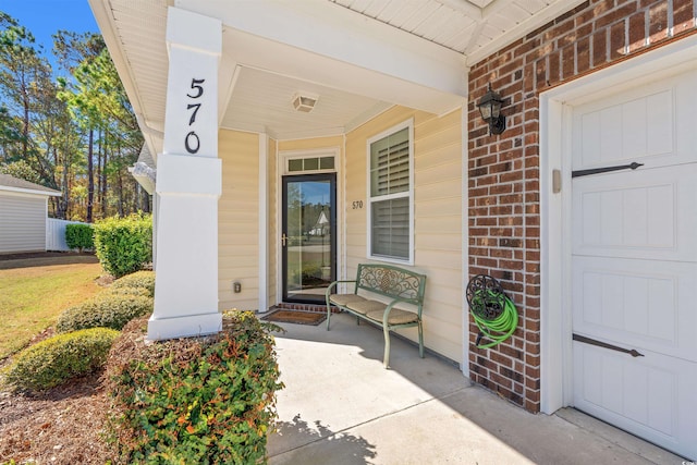entrance to property with a porch, brick siding, and a garage