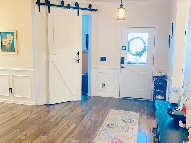 foyer entrance with crown molding, wood finished floors, a barn door, and a decorative wall