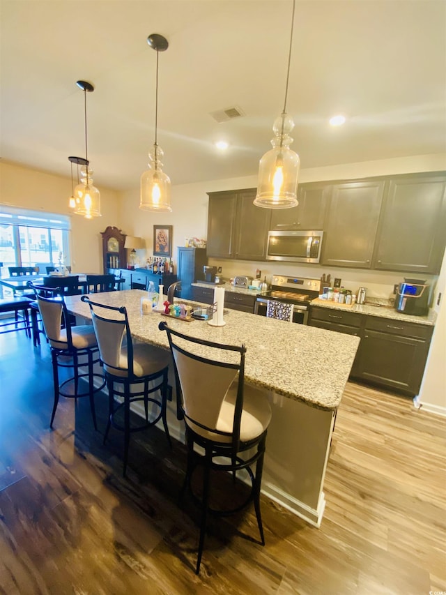 kitchen featuring a center island with sink, wood finished floors, stainless steel appliances, and visible vents