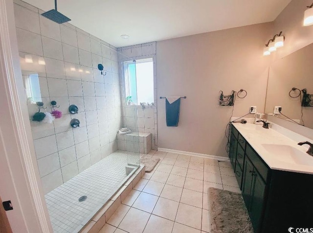 bathroom featuring a tile shower, baseboards, tile patterned flooring, and a sink