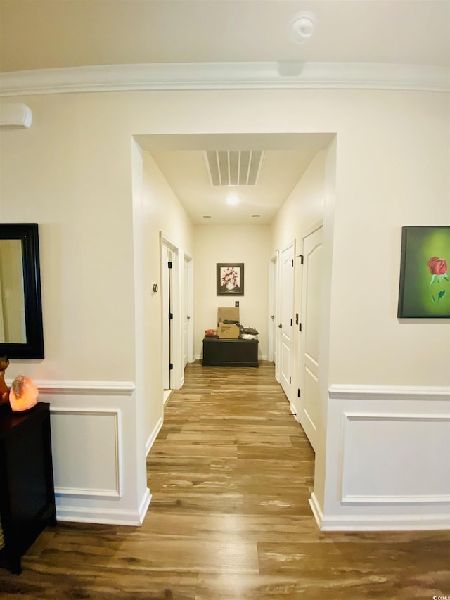 hall with wood finished floors, visible vents, and a wainscoted wall