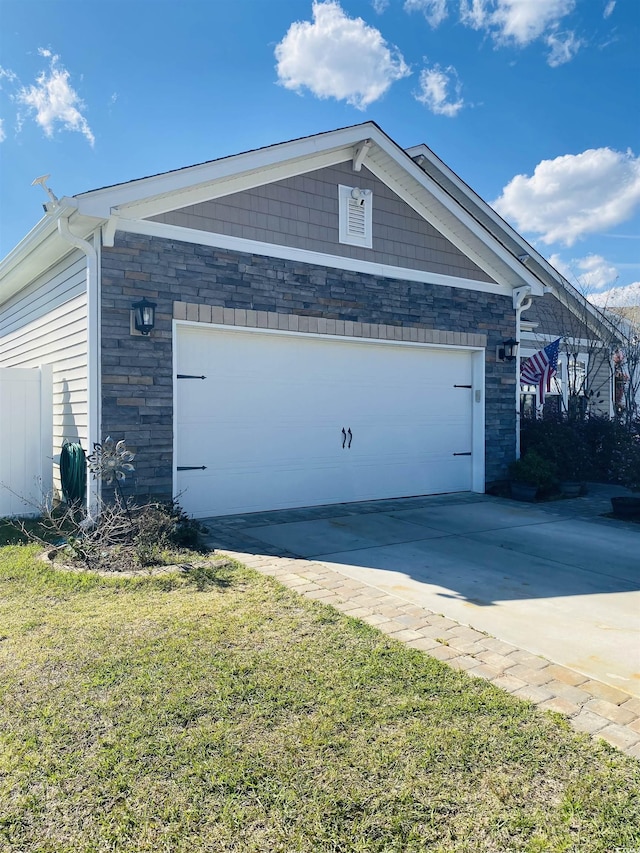 view of side of home with a yard, driveway, stone siding, and a garage