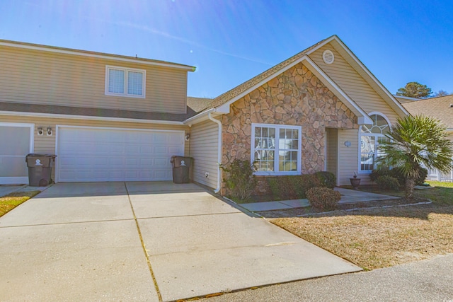 traditional-style home featuring driveway, stone siding, and a garage