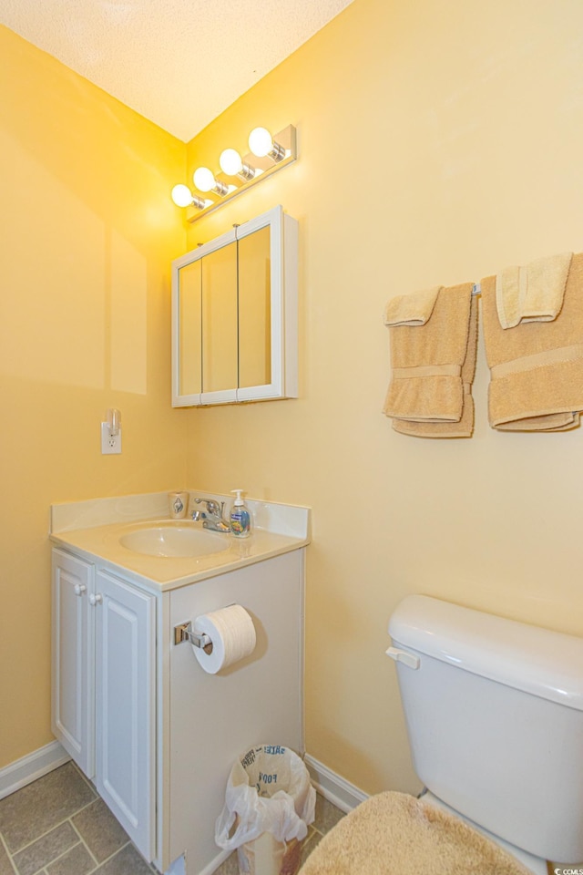 bathroom featuring toilet, baseboards, stone finish floor, and vanity