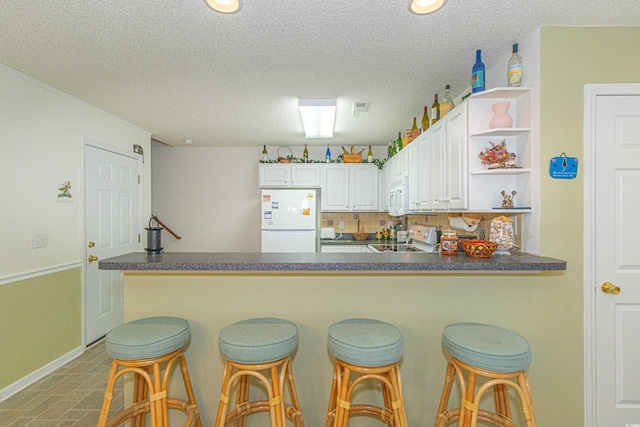 kitchen with white appliances, a peninsula, open shelves, and dark countertops