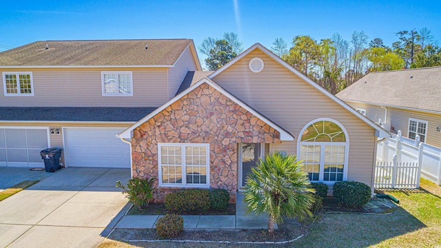 traditional-style house with an attached garage, fence, stone siding, and concrete driveway