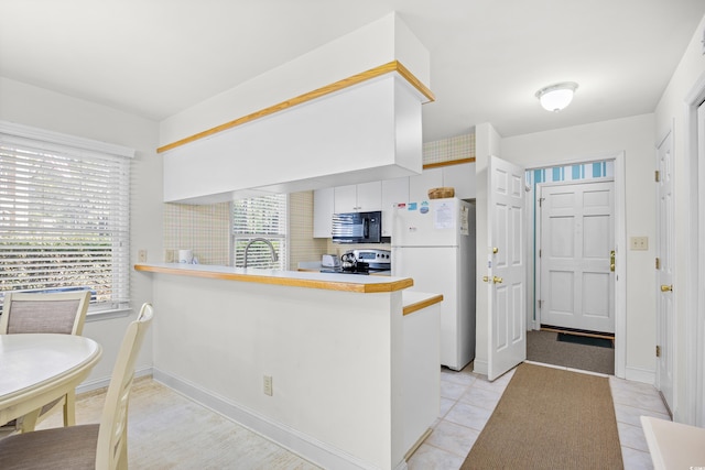kitchen featuring black microwave, freestanding refrigerator, stove, a peninsula, and white cabinetry