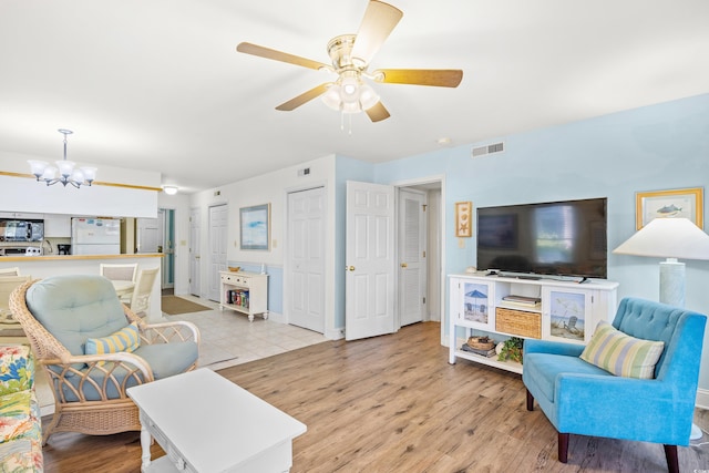living area featuring a chandelier, light wood-type flooring, ceiling fan, and baseboards