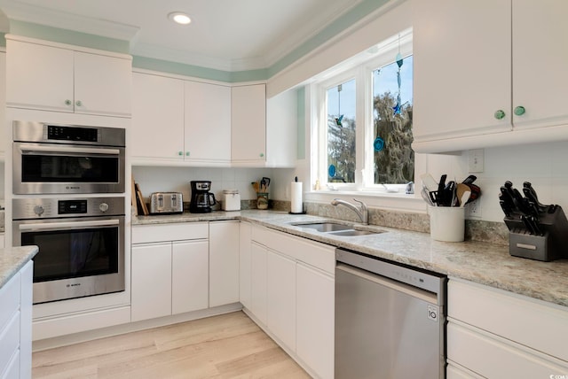 kitchen with white cabinets, crown molding, stainless steel appliances, and a sink