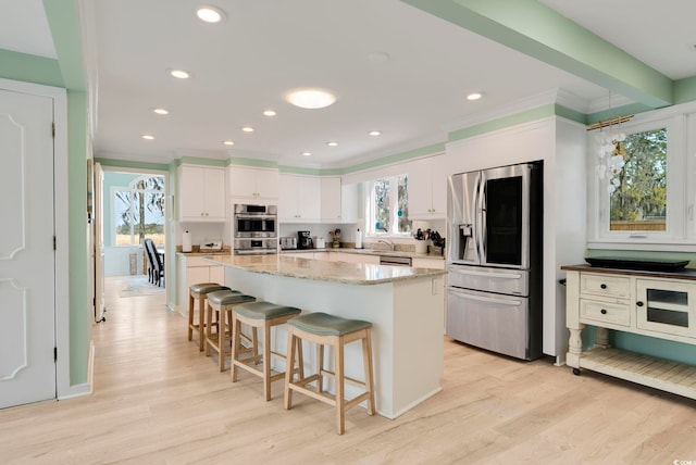 kitchen featuring appliances with stainless steel finishes, light wood finished floors, a breakfast bar, and white cabinetry