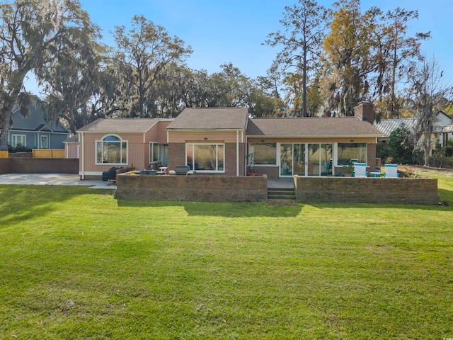 rear view of house with brick siding, a patio area, a lawn, and a chimney