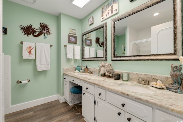 full bath featuring wood finished floors, a sink, a shower with shower door, double vanity, and baseboards