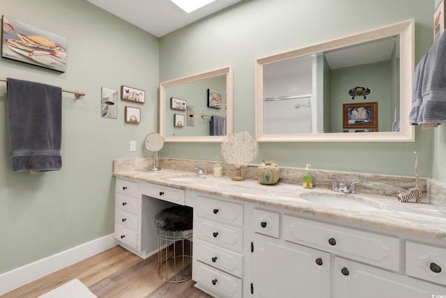 bathroom with wood finished floors, a sink, a shower, double vanity, and baseboards