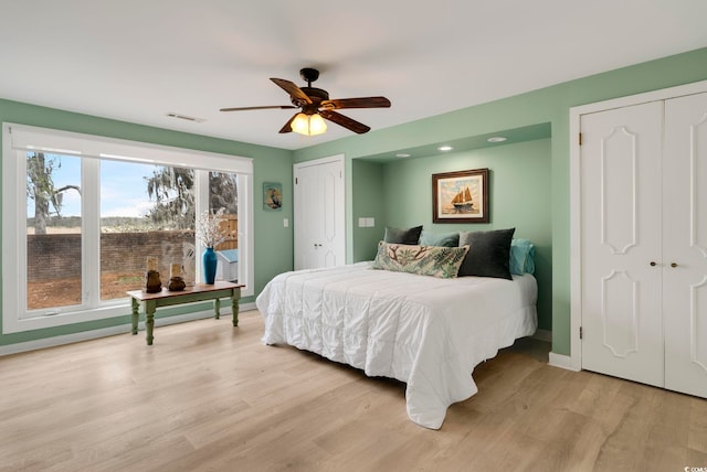 bedroom featuring a ceiling fan, light wood-type flooring, two closets, baseboards, and visible vents