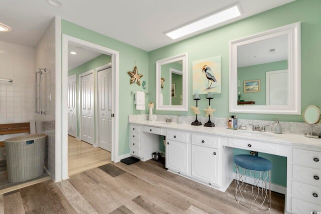 bathroom with wood finished floors, a sink, double vanity, and tiled shower