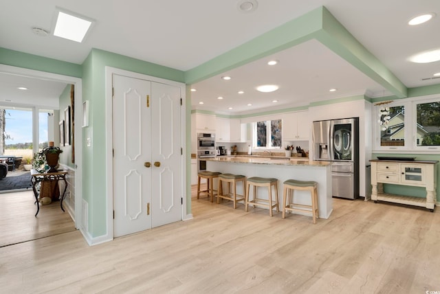 kitchen with a center island, stainless steel fridge, light wood-style flooring, a kitchen bar, and white cabinetry