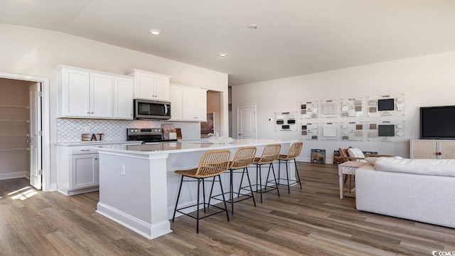 kitchen featuring dark wood-type flooring, white cabinetry, appliances with stainless steel finishes, a kitchen island with sink, and open floor plan