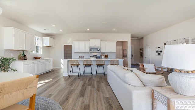living room featuring baseboards, recessed lighting, light wood-style floors, and lofted ceiling
