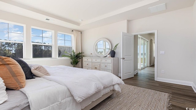 bedroom featuring a tray ceiling, baseboards, dark wood finished floors, and visible vents