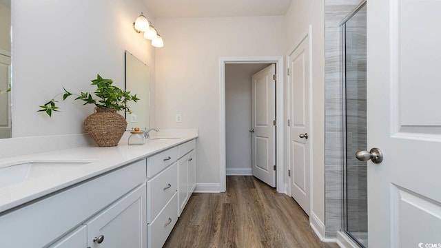 full bath with a sink, tiled shower, double vanity, and wood finished floors
