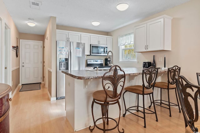1425 N Waccamaw Dr Unit 123, Garden City Beach, SC 29576 - kitchen featuring appliances with stainless steel finishes, a peninsula, light wood-type flooring, a kitchen breakfast bar, and a textured ceiling