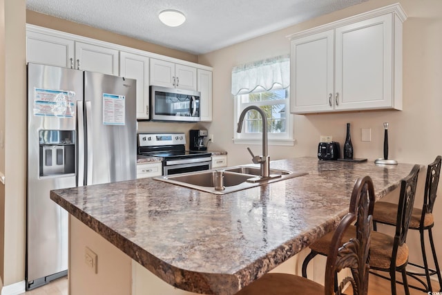 1425 N Waccamaw Dr Unit 123, Garden City Beach, SC 29576 - kitchen featuring stainless steel appliances, a peninsula, a sink, a kitchen bar, and white cabinets