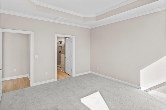 unfurnished bedroom with carpet floors, crown molding, a raised ceiling, baseboards, and connected bathroom