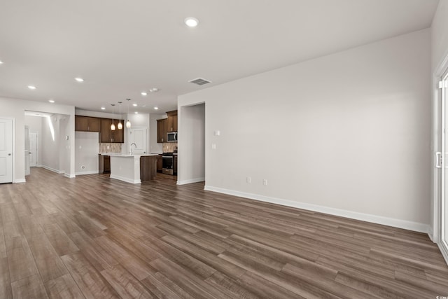 unfurnished living room with baseboards, dark wood-type flooring, recessed lighting, and a sink