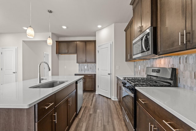 kitchen with appliances with stainless steel finishes, a sink, dark wood-style floors, decorative backsplash, and an island with sink