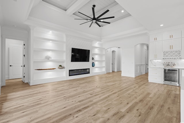 unfurnished living room with beverage cooler, arched walkways, ornamental molding, light wood-style floors, and built in features