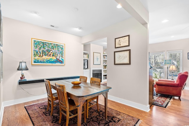 dining area featuring baseboards, light wood-type flooring, recessed lighting, and a fireplace