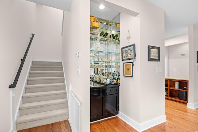 bar featuring bar, baseboards, light wood finished floors, and stairs
