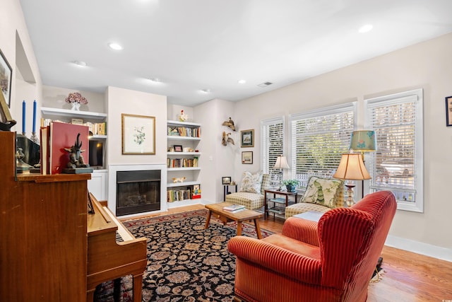 living room featuring a glass covered fireplace, recessed lighting, visible vents, and wood finished floors