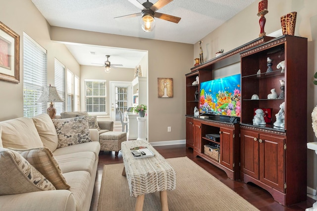 living area featuring a ceiling fan, dark wood-style flooring, a textured ceiling, and baseboards
