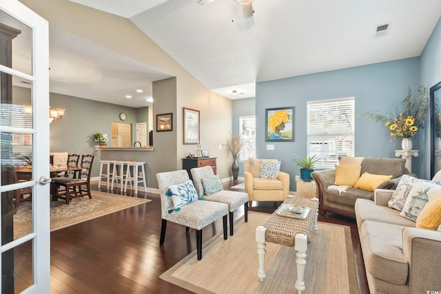 living area with hardwood / wood-style flooring, visible vents, baseboards, vaulted ceiling, and ceiling fan with notable chandelier