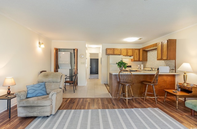 kitchen with stacked washer and dryer, light countertops, a peninsula, brown cabinetry, and under cabinet range hood