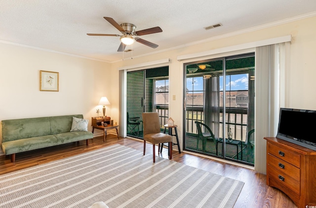 living room with ornamental molding, visible vents, ceiling fan, and wood finished floors