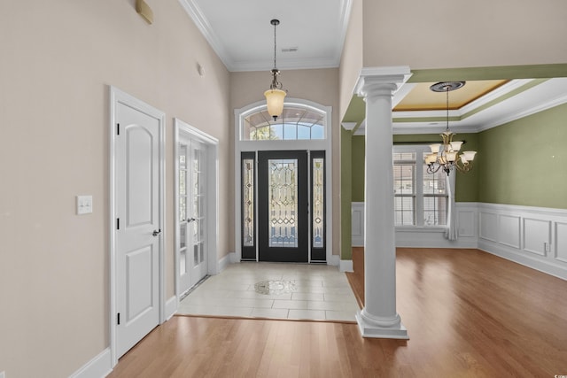 foyer with decorative columns, wood finished floors, an inviting chandelier, and ornamental molding