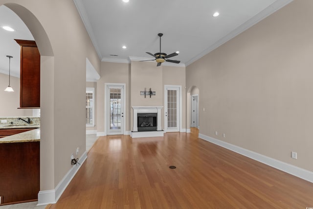 unfurnished living room with recessed lighting, a ceiling fan, arched walkways, crown molding, and light wood-style flooring