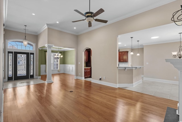 unfurnished living room featuring arched walkways, light wood-style flooring, ceiling fan with notable chandelier, and ornate columns