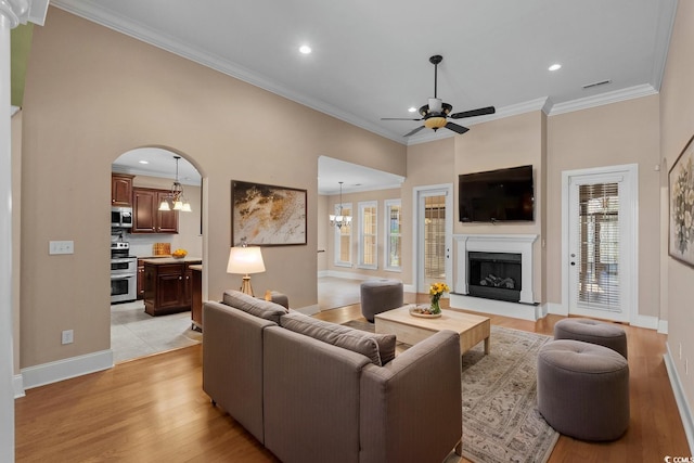 living room with light wood-style floors, a fireplace with raised hearth, a healthy amount of sunlight, and ceiling fan with notable chandelier