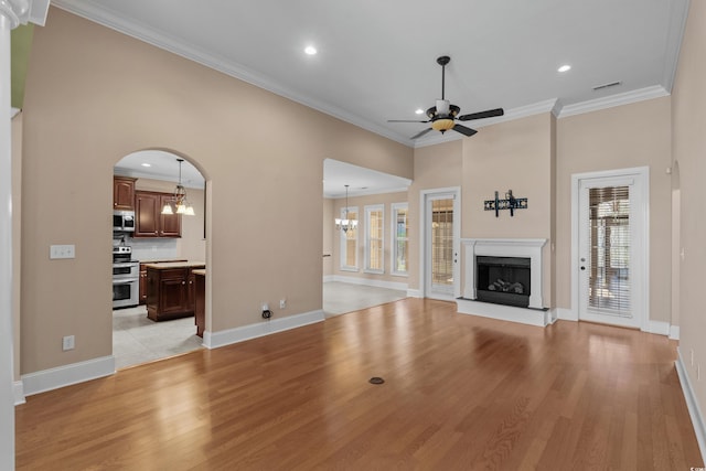 unfurnished living room featuring ceiling fan with notable chandelier, a wealth of natural light, and light wood finished floors