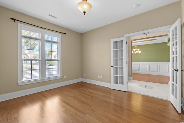unfurnished room featuring an inviting chandelier, wood finished floors, visible vents, and french doors