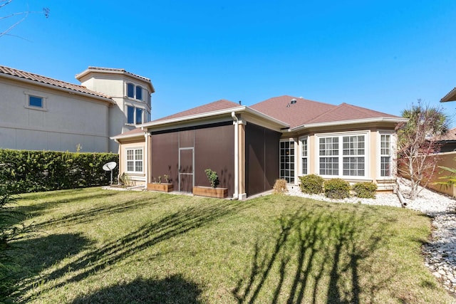 rear view of house featuring a sunroom, stucco siding, and a lawn
