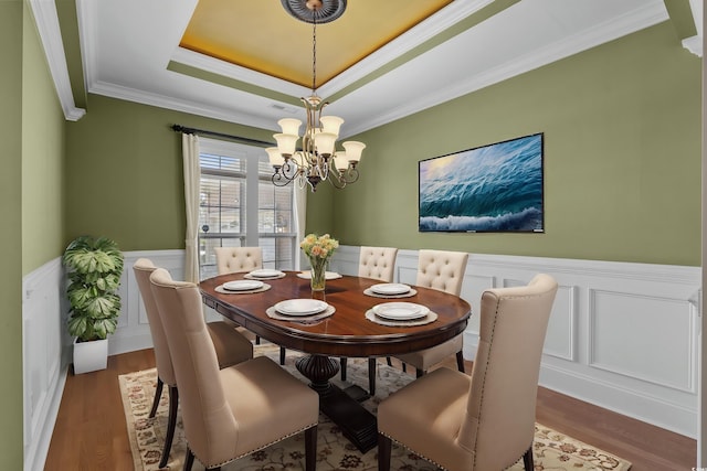 dining room featuring a decorative wall, wood finished floors, a chandelier, and a raised ceiling